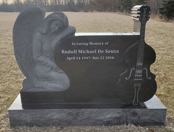 Black granite headstone with a sculpted kneeling angel and a carved three-dimensional bass guitar