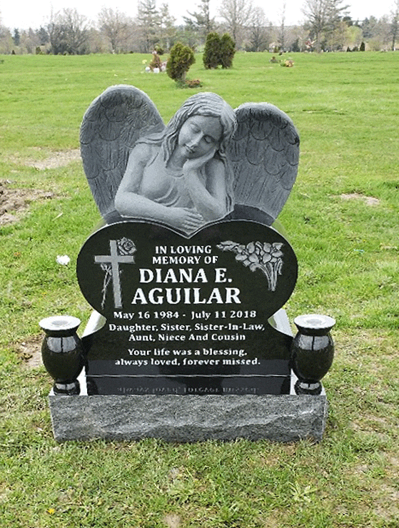 Black granite heart-shaped headstone with a sculpted leaning angel, an engraved cross and calla lilies, shown with matching vases