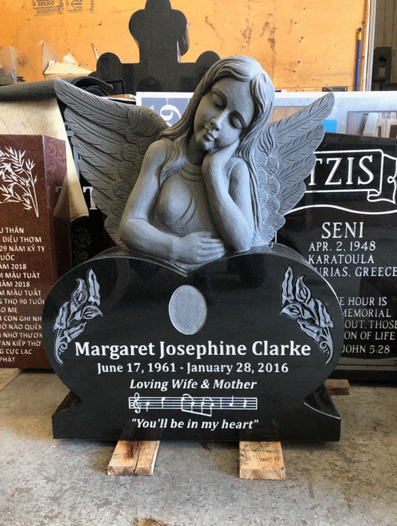 Black granite heart-shaped headstone with a sculpted resting cherub, carved roses, and engraved musical notes
