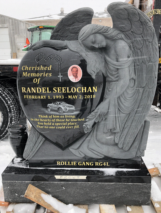 Black granite heart-shaped headstone with a sculpted angel leaning over it, a portrait medallion, and an engraved rosary