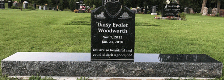 Black granite bench memorial with an engraved swan, heart, and sunrise on a grey granite base