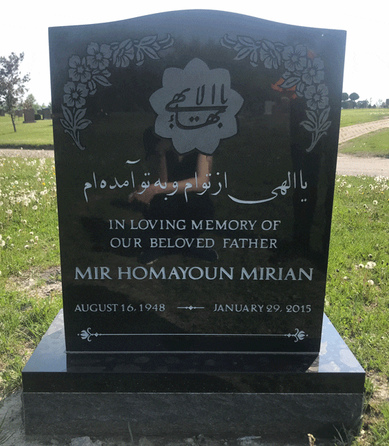 Black granite upright headstone with carved floral corners and an engraved Baha'i emblem, English and Persian inscription