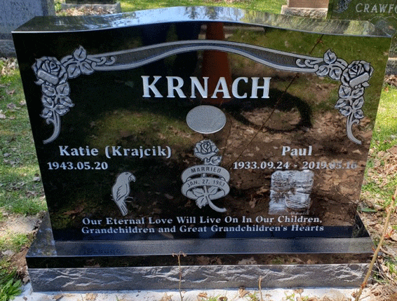 Black granite upright headstone with carved rose-vine corners, a portrait medallion, and a wedding-rings emblem
