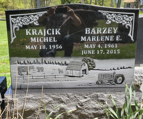 Black granite upright headstone with floral corners and an engraved farm scene with a barn, tractor, and cattle