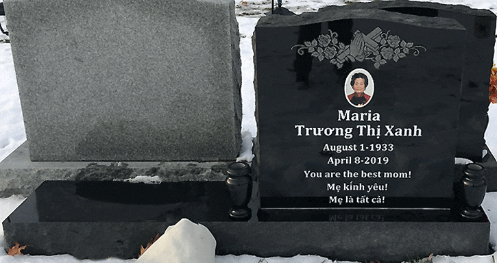 Black granite upright headstone with engraved praying hands, a floral spray, and a portrait medallion, Vietnamese inscription