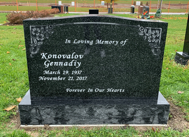 Dark granite upright headstone with engraved floral corners and a memorial inscription