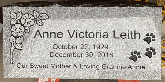 Grey granite flat grave marker with carved morning-glory flowers and paw prints