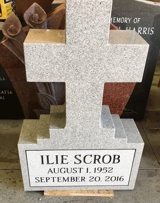 Light grey granite cross-shaped headstone with calla lily carvings and an engraved name panel