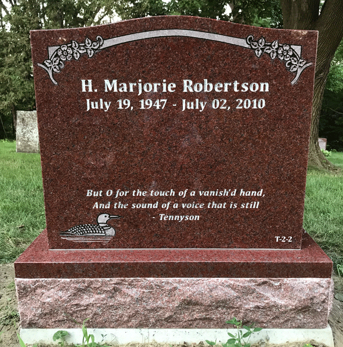 Red granite upright headstone with a floral scroll border and an engraved loon