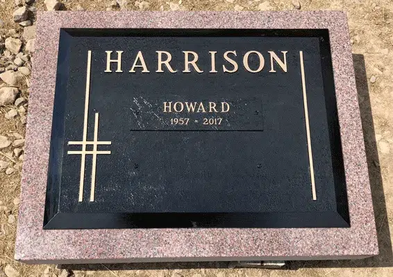 Black flat grave marker with thin gold lines forming a minimalist cross, raised family name and name plate on pink granite