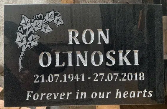 Black granite flat grave marker with a carved ivy leaf spray in the top corner, a name in capitals, dates and an epitaph