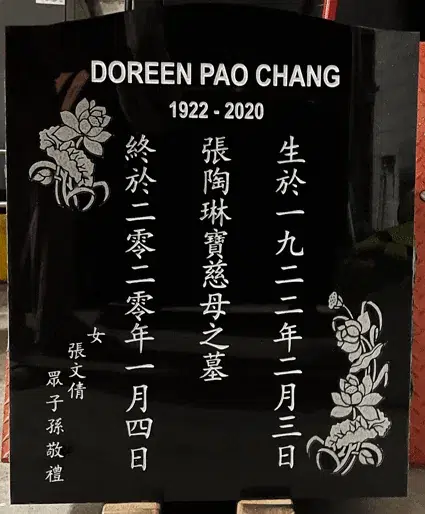 Black granite serpentine top headstone with English and vertical Chinese inscriptions and etched roses in two corners