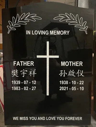 Black granite upright headstone with an etched Latin cross between two Chinese names and leaf sprays in the upper corners