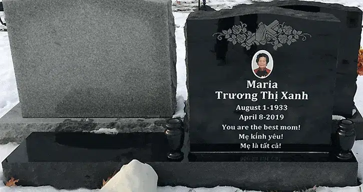 Black granite upright headstone with engraved praying hands, a floral spray, and a portrait medallion, Vietnamese inscription