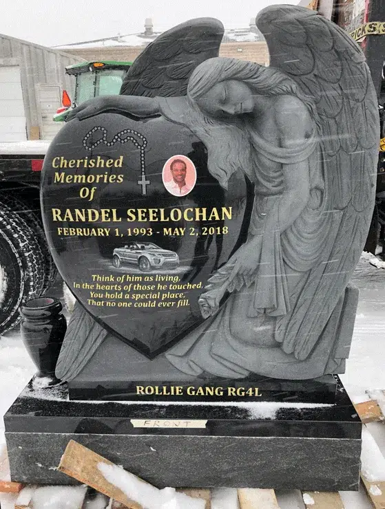 Black granite heart shaped headstone with a grey sculpted angel leaning over it, gold lettering and an oval portrait