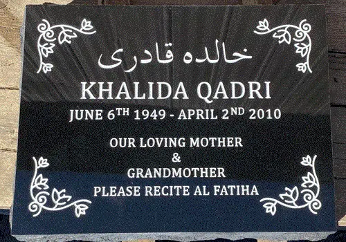 Black granite flat grave marker with floral vine artwork in each corner, an Arabic script line and an English inscription