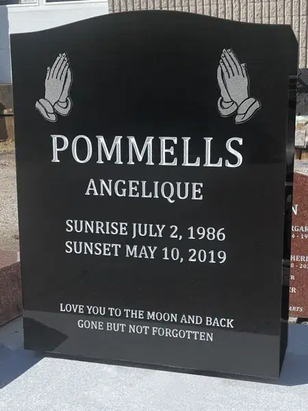 Black granite serpentine top headstone with praying hands etched in both upper corners above a name, dates and epitaph