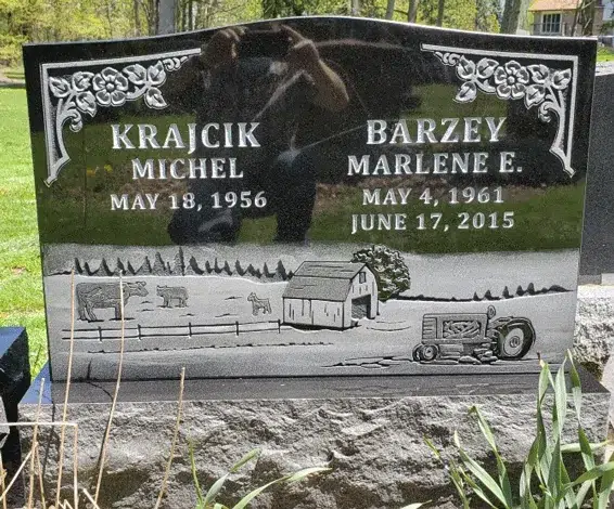 Black granite upright headstone with floral corners and an engraved farm scene with a barn, tractor, and cattle