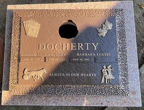Bronze companion marker on pink granite with playing cards, maple leaves, a harness racing horse and a dancing couple