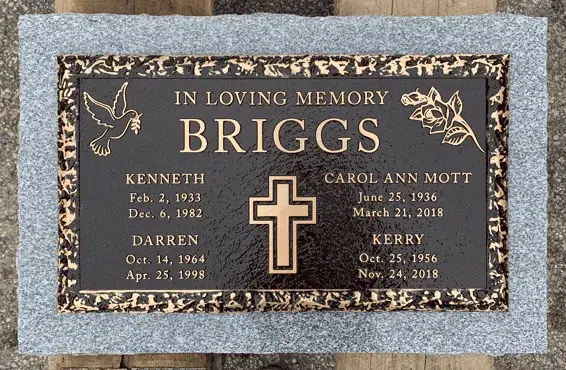 Bronze family marker on a grey granite base with a raised cross, a dove, roses, a textured border and four names with dates