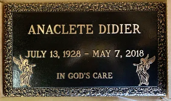 Bronze grave marker with a stippled border, two angel figures in the lower corners and a raised name and dates