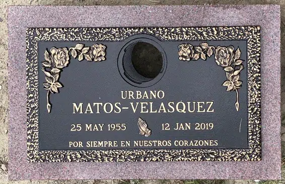 Bronze grave marker on a pink granite base with a center vase, rose corners, praying hands and a raised name with dates