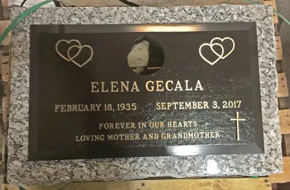 Bronze grave marker with double heart emblems, a round vase opening at the top and a small cross on grey granite