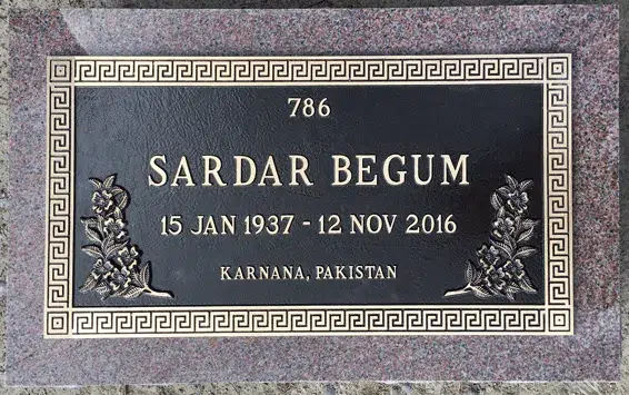 Bronze grave marker with a Greek key border, floral corner sprays and raised lettering on a red granite base