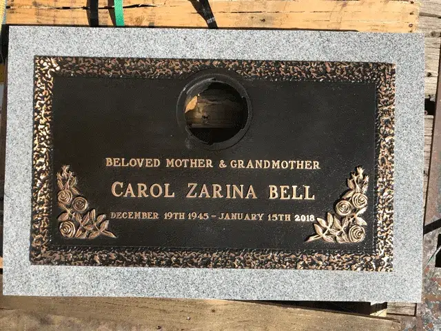Bronze grave marker with a round vase opening, rose clusters in the lower corners and a textured rim on grey granite