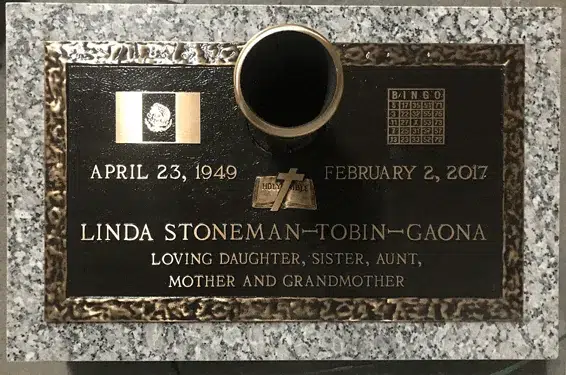 Bronze grave marker with a standing centre vase, flag and bingo card emblems and an open Bible with cross on grey granite
