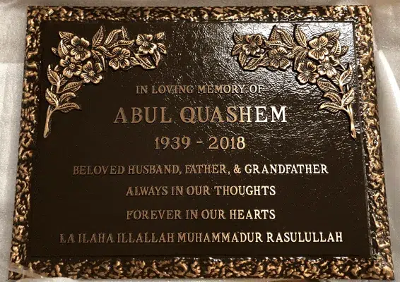 Bronze memorial marker with a stippled border, flower clusters in the top corners and raised lettering with a name and years