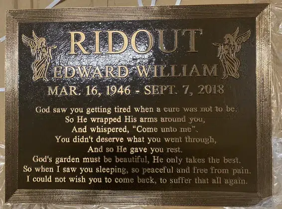 Bronze memorial plaque with a stepped border, angels in the top corners, a raised family name, dates and a memorial poem