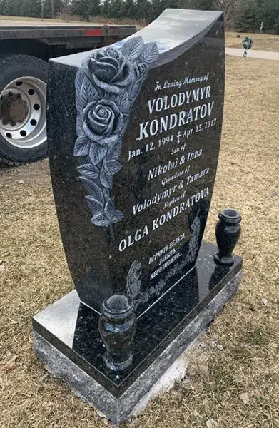 Side view of a curved black granite upright headstone with carved roses, two granite vases and an engraved inscription