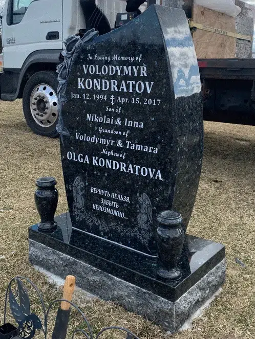 Curved black granite upright headstone with carved roses, an engraved inscription, angel figures and two granite vases