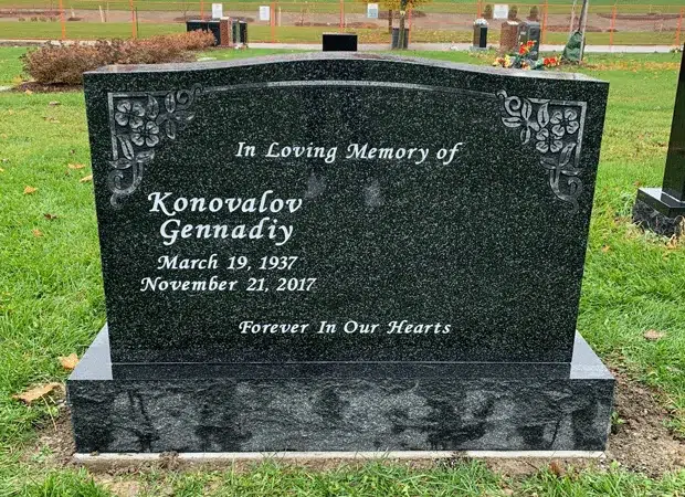 Dark granite upright headstone with engraved floral corners and a memorial inscription