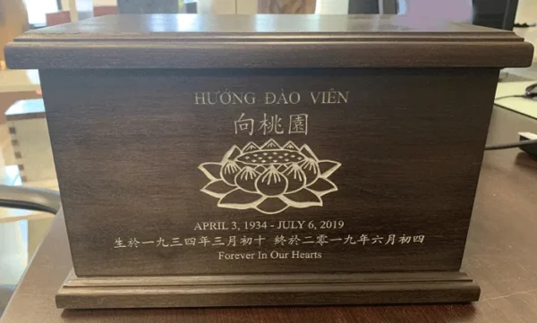 Engraved Wood Urn with Lotus Flower Dark brown wood urn engraved with a lotus flower, a name in Vietnamese and Chinese, dates and a short epitaph