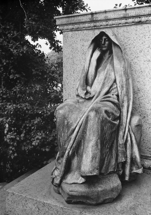 Close up of a hooded bronze figure seated on a rock, one hand raised to its chin, Rock Creek Cemetery, Washington DC