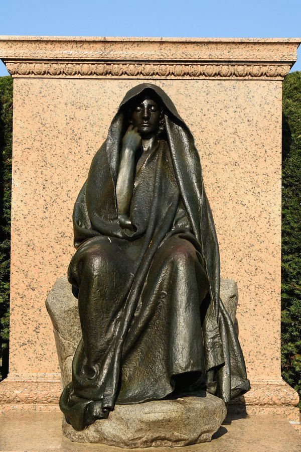 Front view of a hooded bronze figure seated on a boulder before a pink granite block, Rock Creek Cemetery, Washington DC