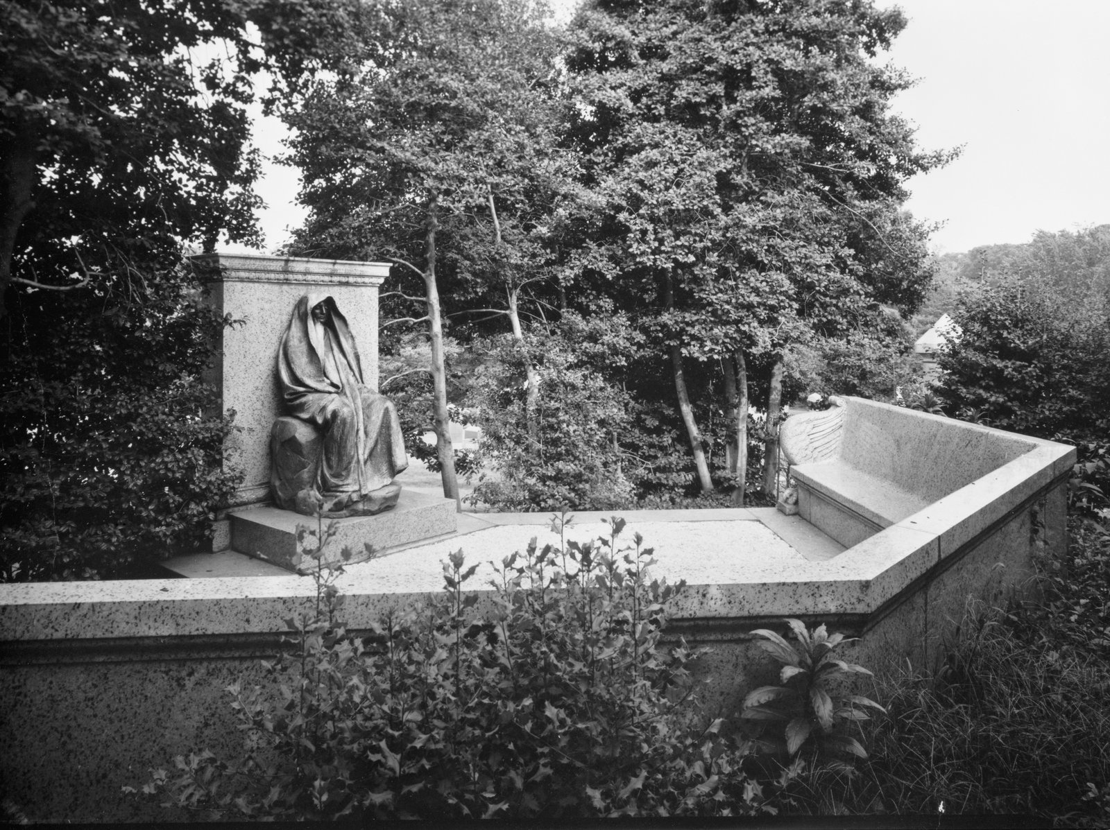 Hooded bronze figure seated against a stone block in a walled plot with a curved bench, Rock Creek Cemetery, Washington DC
