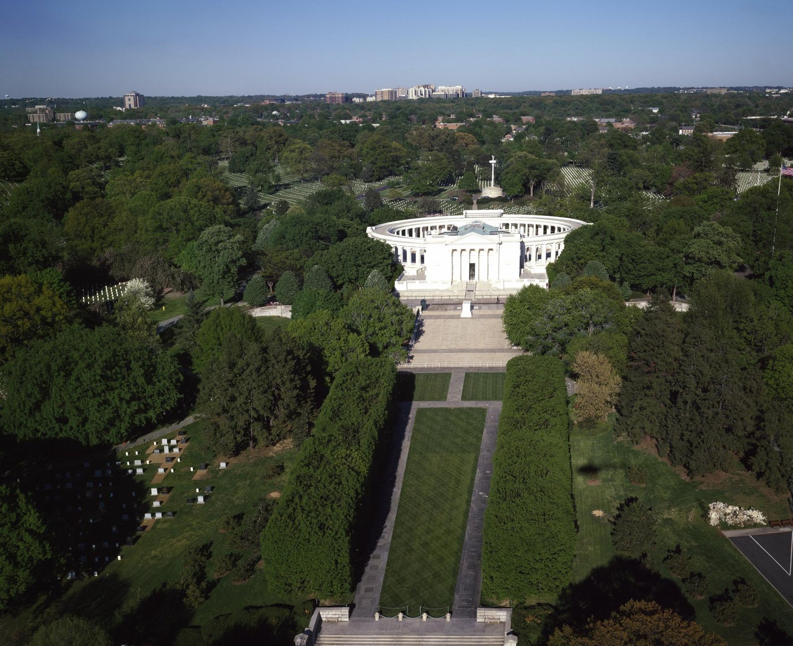 Aerial view of the white columned Memorial Amphitheater at Arlington National Cemetery with a long lawn and headstone rows