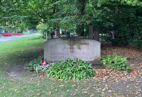 Upright light grey headstone under a large tree at Mount Pleasant Cemetery, Toronto, with small stones along its top