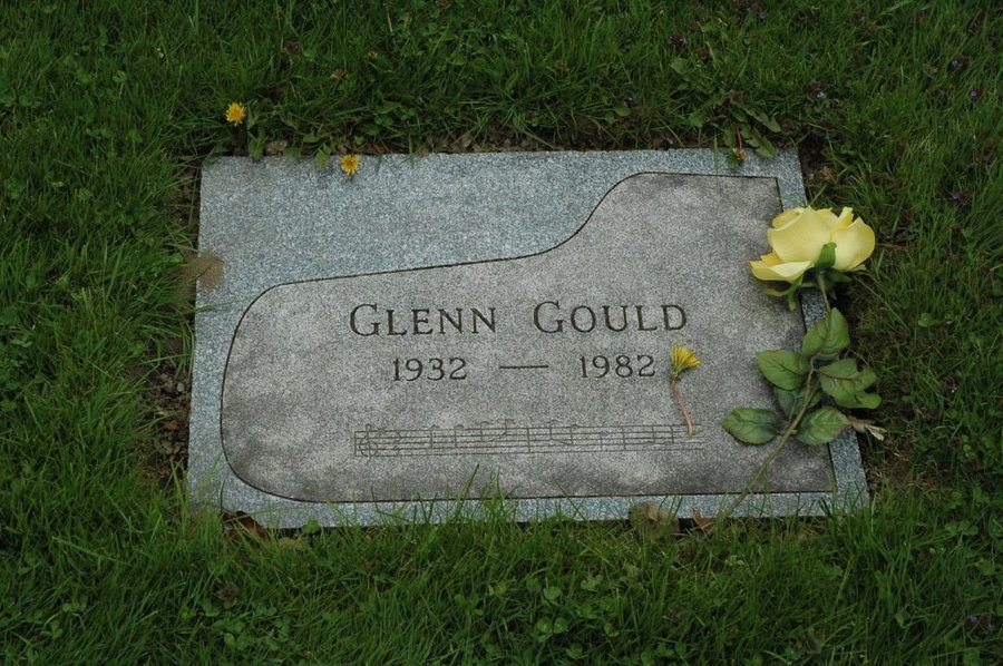 Flat grey granite marker cut with the outline of a grand piano, set flush in grass at Mount Pleasant Cemetery, Toronto