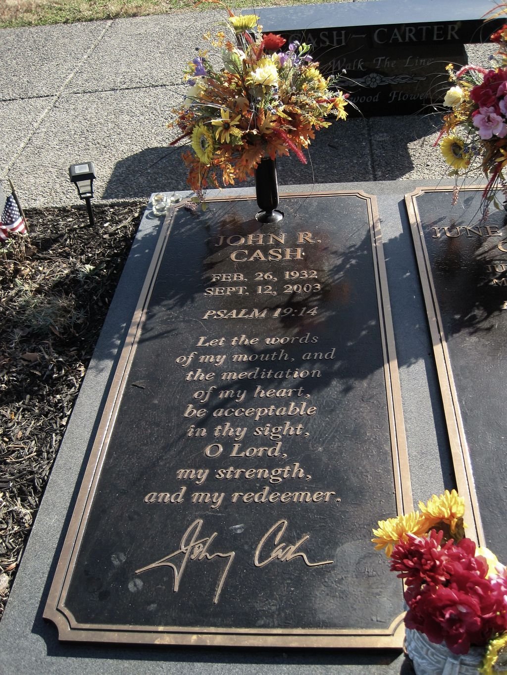 Two matching flat bronze markers with flowers and a dark stone bench behind at Hendersonville Memory Gardens, Tennessee