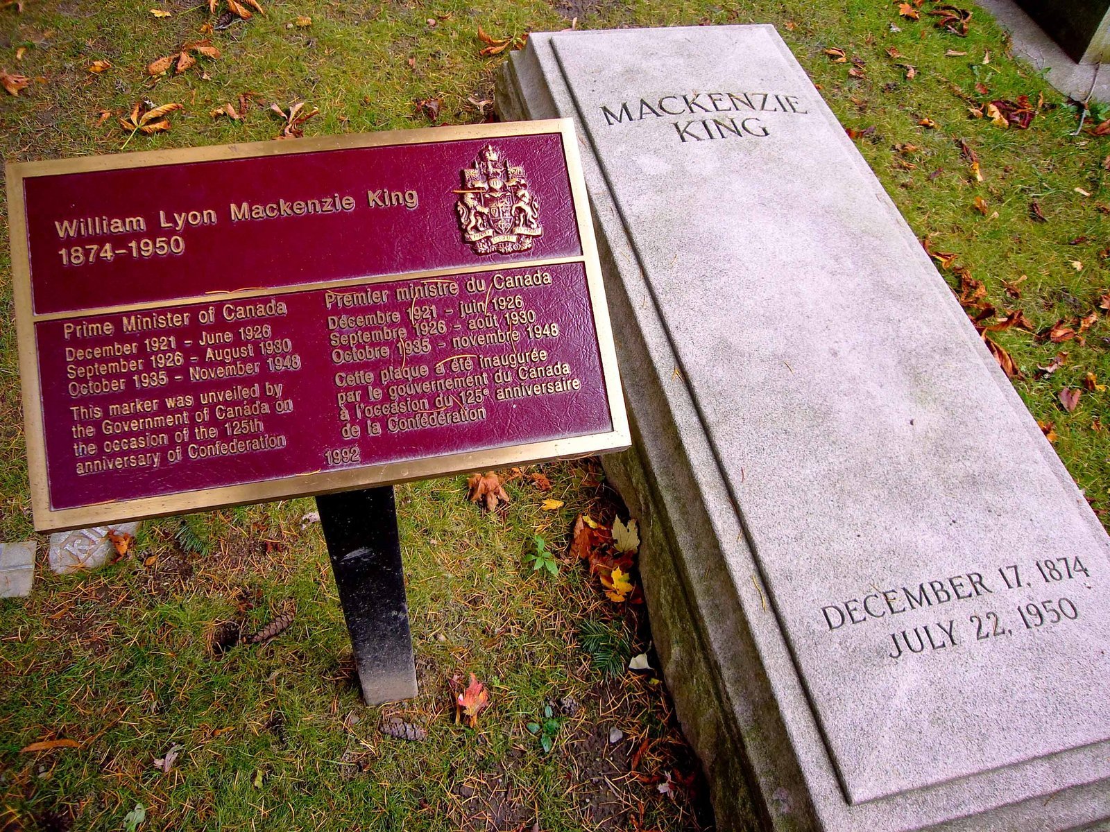 Flat grey granite slab with carved lettering beside a dark red plaque on a post at Mount Pleasant Cemetery, Toronto