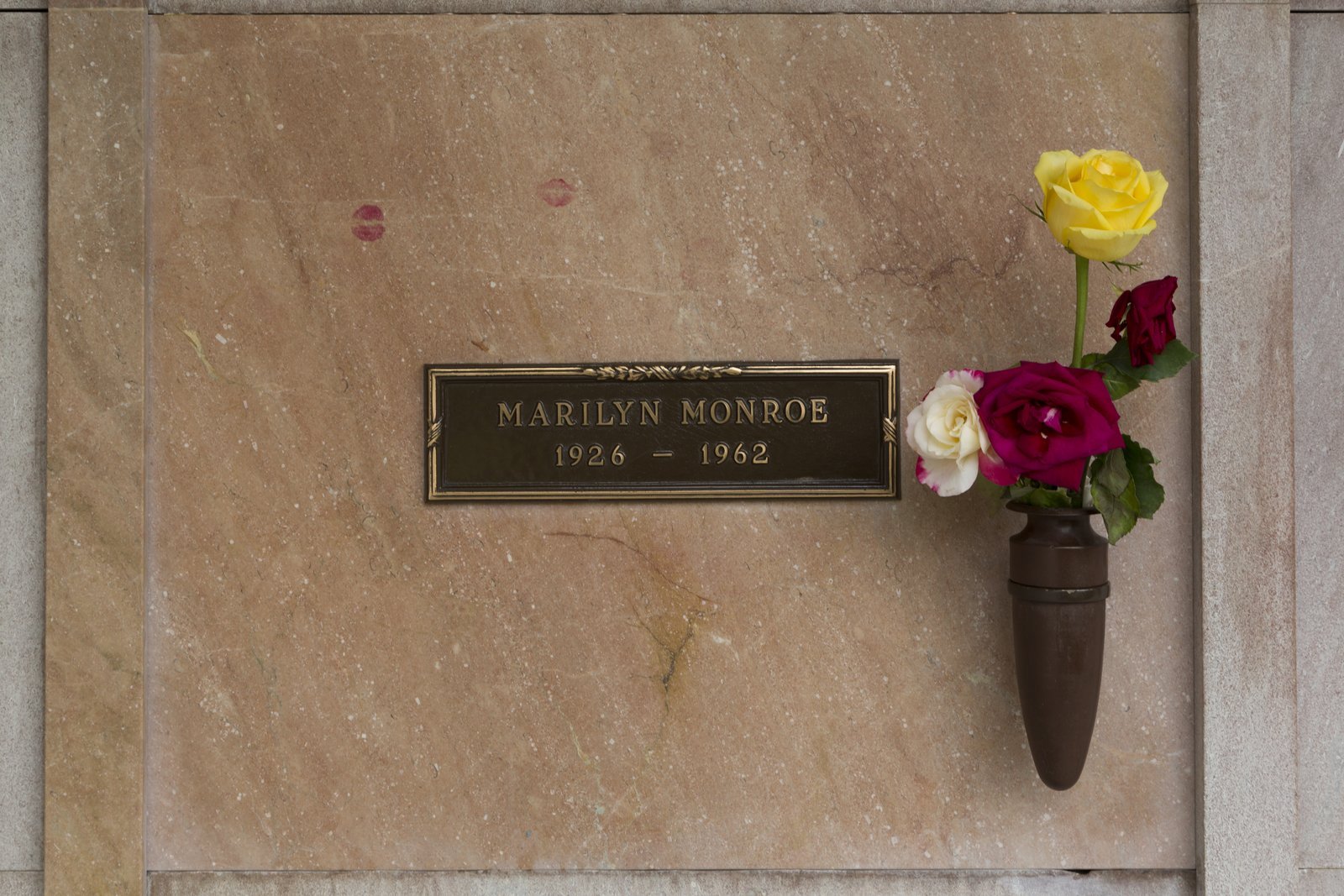 Close view of a pink stone wall crypt with a bronze name plaque and roses in a wall vase, Westwood Village Memorial Park