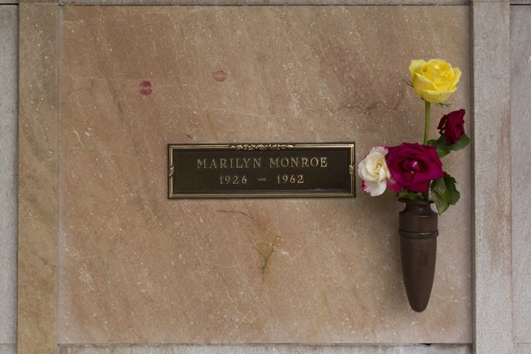 Pink stone wall crypt front with a small bronze plaque and a vase of roses at Westwood Village Memorial Park, Los Angeles