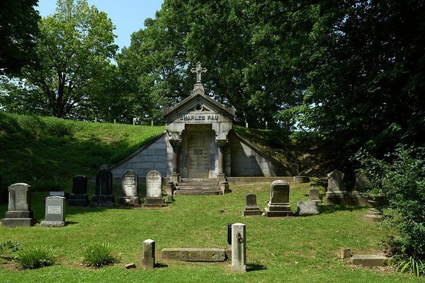 Grey stone mausoleum set into a grassy hillside with small headstones in front at Mount Hope Cemetery, Rochester, New York
