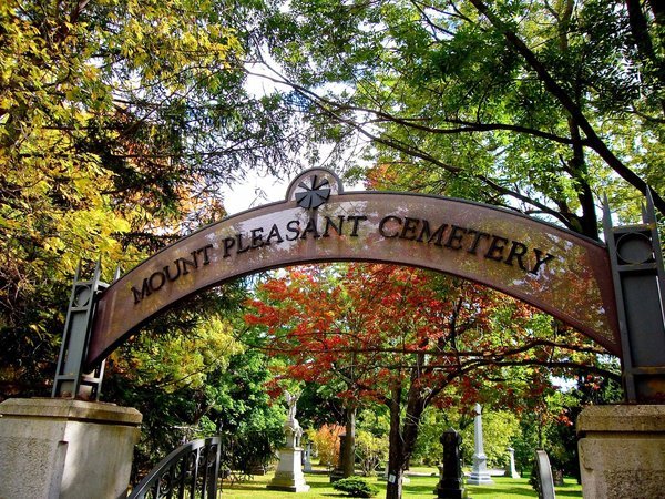 Entrance arch at Mount Pleasant Cemetery in Toronto, with a metal gate, autumn trees and monuments beyond