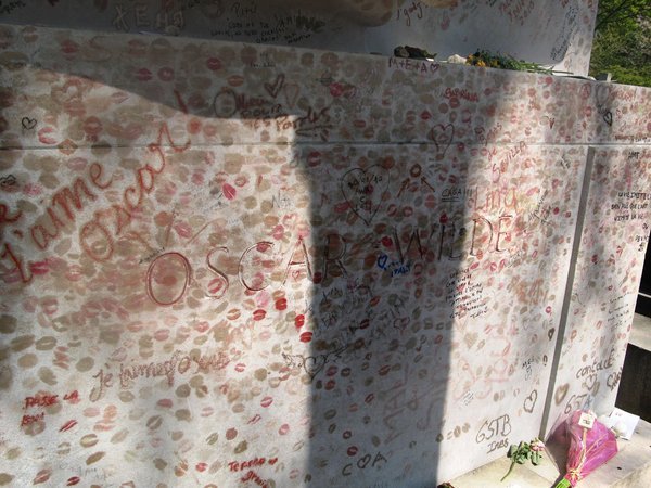 Lipstick kisses and handwritten notes covering a pale stone tomb at Père Lachaise Cemetery, Paris