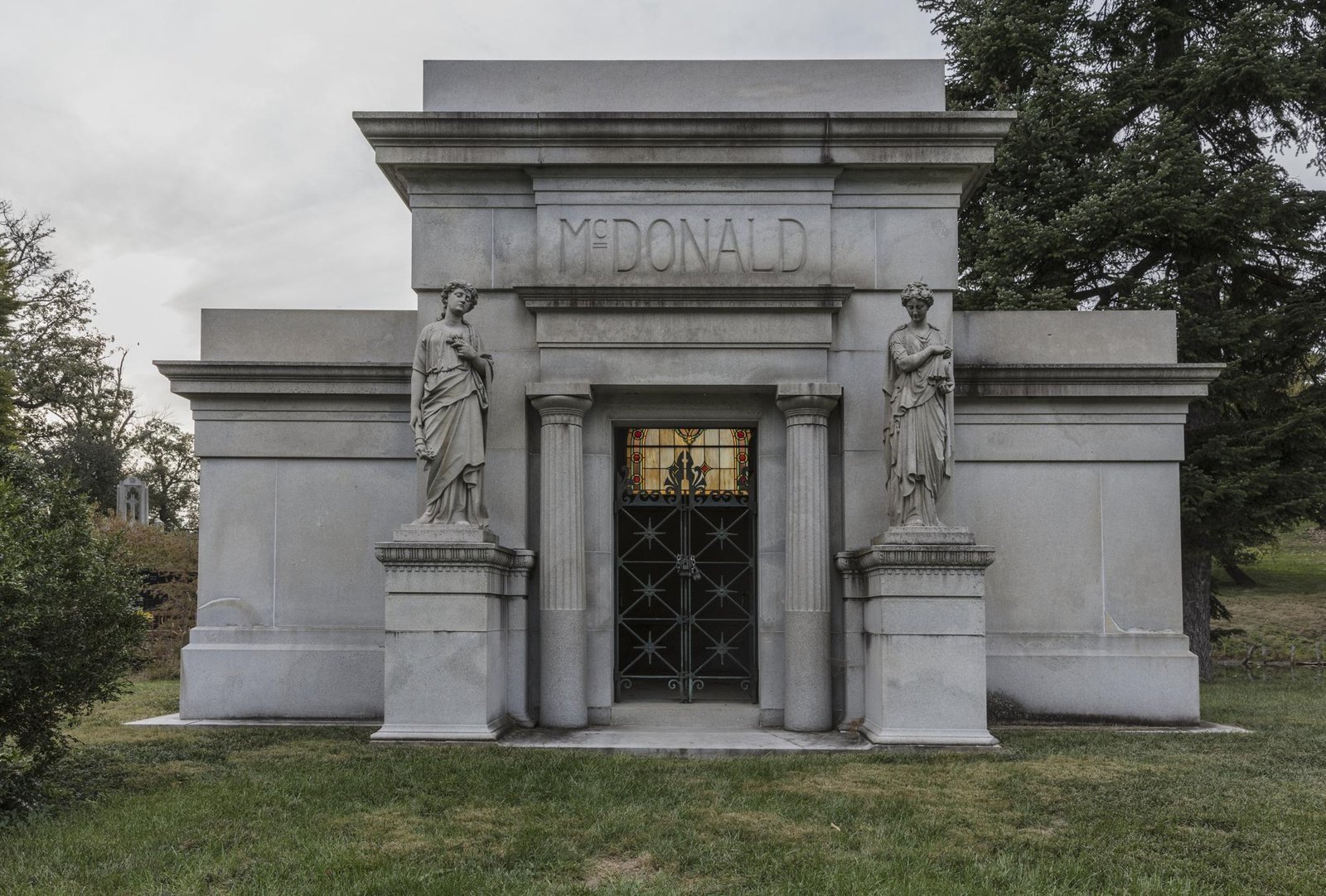 Grey stone mausoleum with two statues, columns and a metal gate at Spring Grove Cemetery in Cincinnati, Ohio